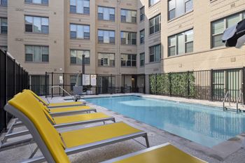 A pool with yellow sun loungers in front of a building.